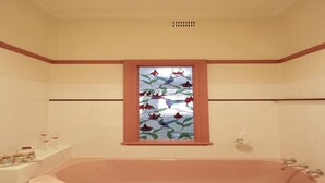 A bathroom with a large bathtub, a window with a stained glass design, and a shelf with toiletries. - Homely 2-Bed Cottage Near Tenterfield Centre (Tenterfield)