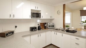 A modern kitchen with white cabinets, a microwave, toaster, and a clock on the wall. - Homely 2-Bed Cottage Near Tenterfield Centre (Tenterfield)