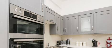 A modern kitchen with grey cabinets, a double oven, a sink, and a countertop with various appliances.