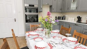 Une cuisine avec des meubles gris, un four double et une table à manger dressée pour six personnes, avec des assiettes à pois rouges et blancs.