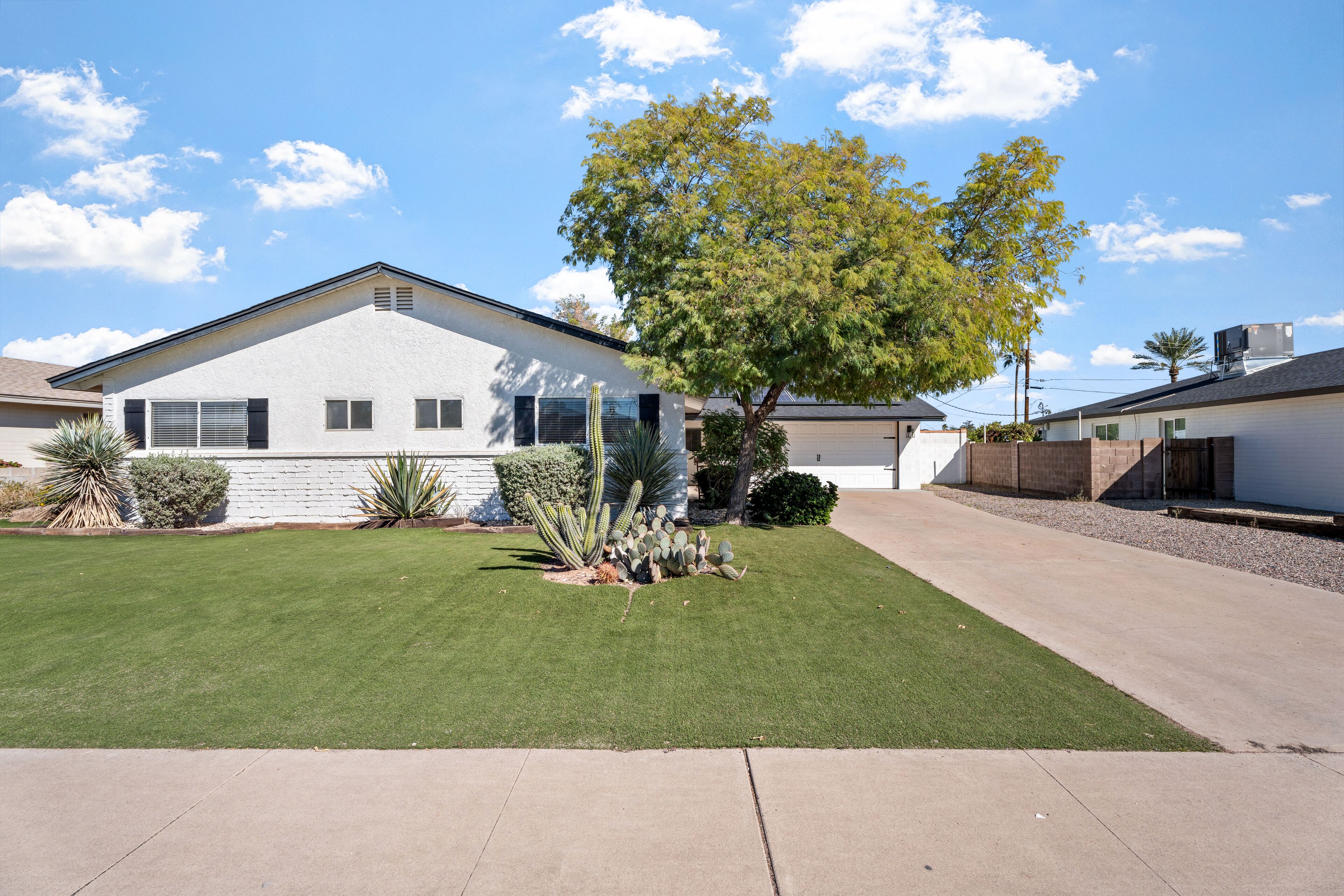 A single-story house with a well-maintained lawn, a large tree, and a clear sky.