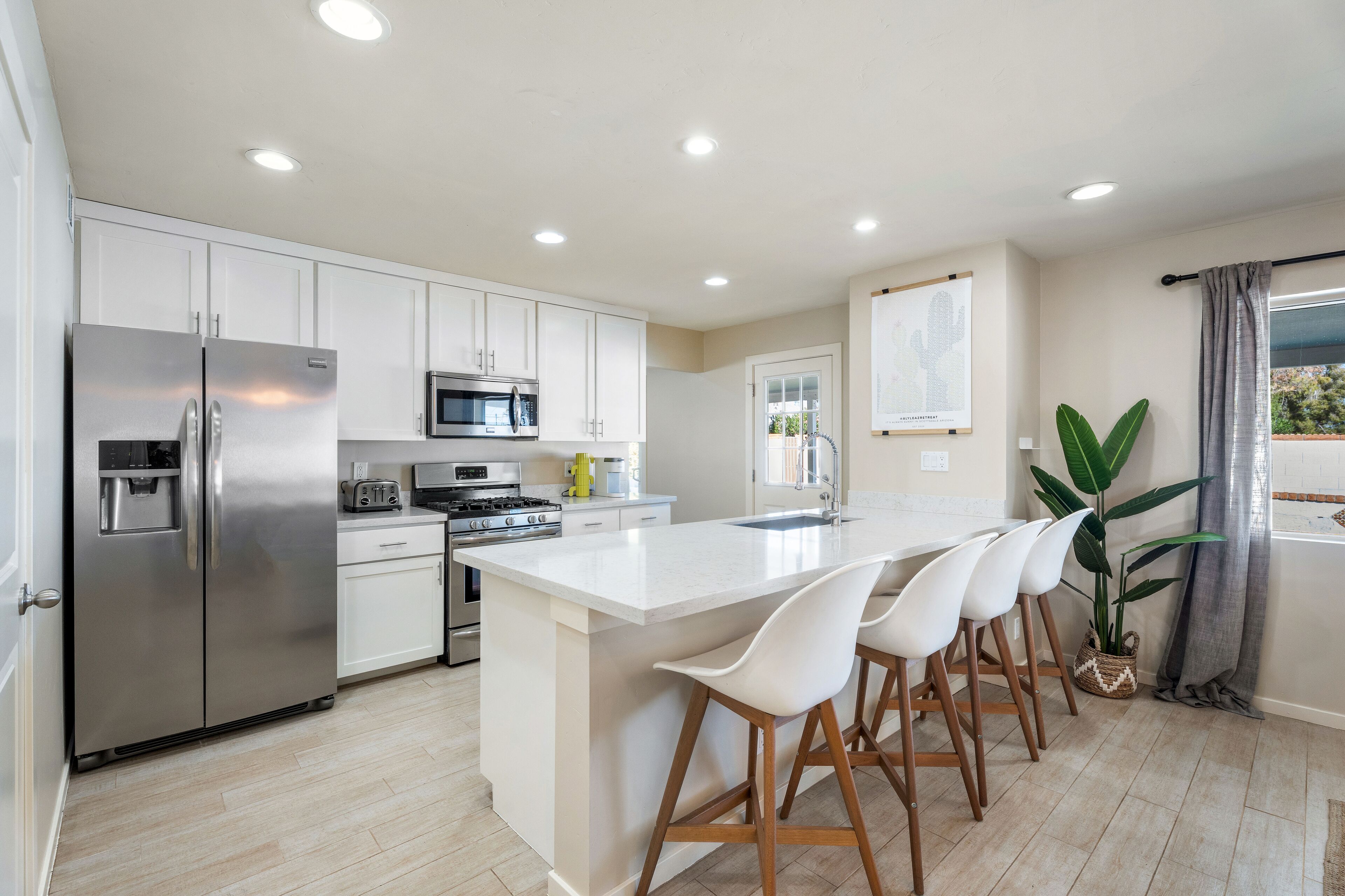 A modern kitchen with white cabinets, stainless steel appliances, and a central island with bar stools.