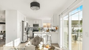 Een moderne keuken met roestvrijstalen apparatuur, een eethoek met een ronde tafel, en grote schuifpuien naar een terras.