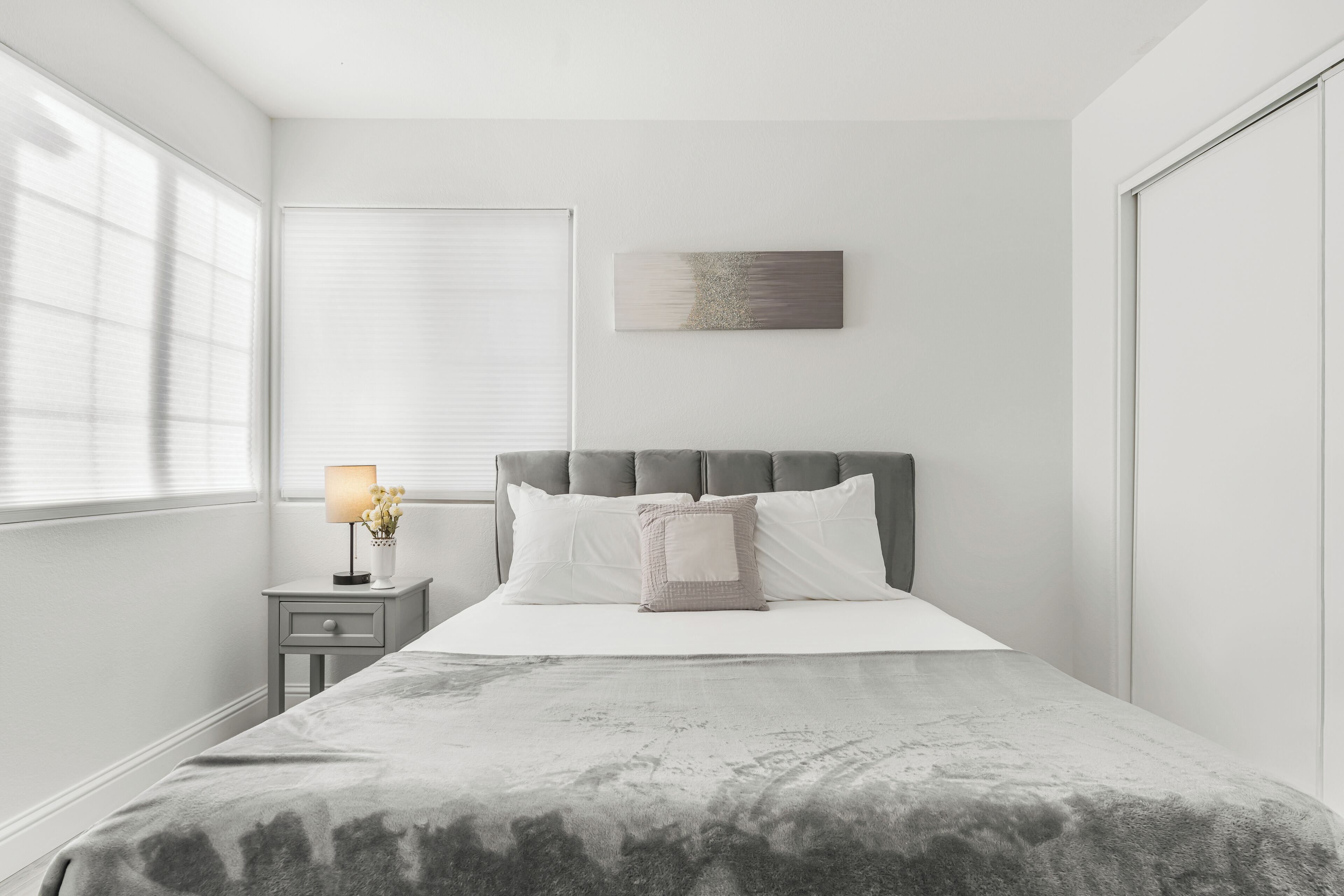 A bedroom with a bed, a nightstand with a lamp, and a window with blinds.