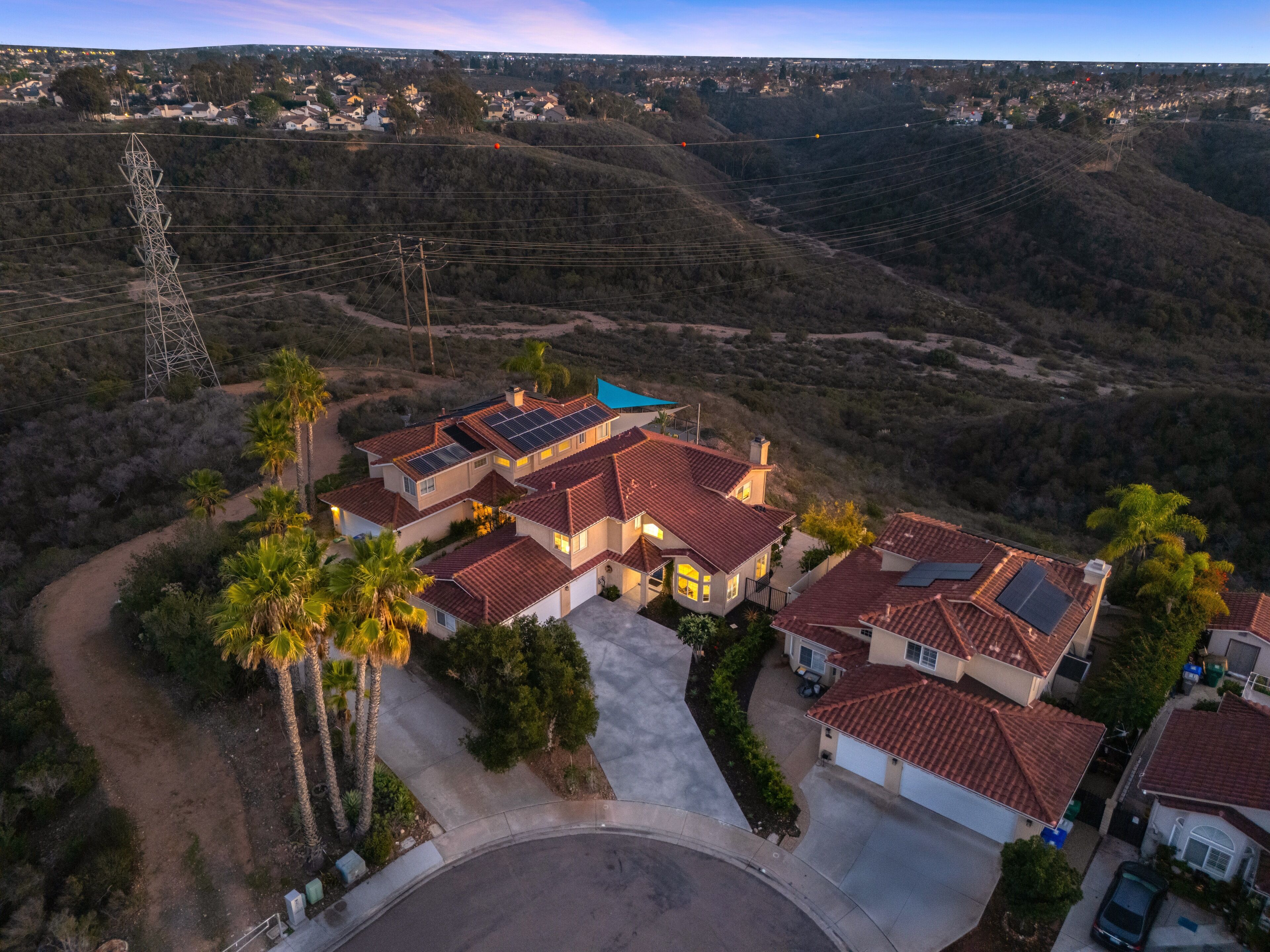 Aerial view of the large Mediterranean-style home and surrounding hilly landscape at sunset/dusk.