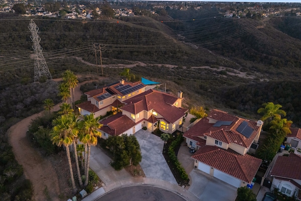 Aerial view of the large Mediterranean-style home and surrounding hilly landscape at sunset/dusk.
