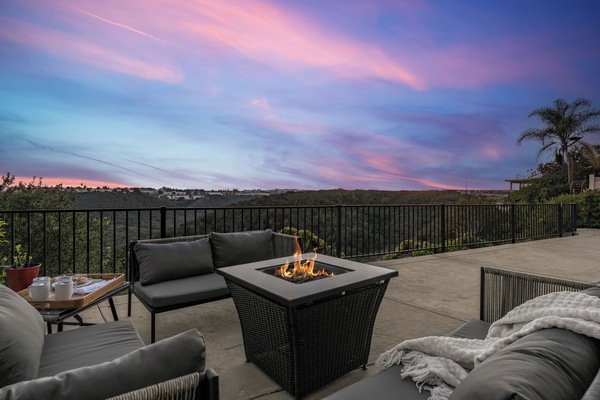 Outdoor patio with a fire pit table and seating, overlooking the scenic canyon view at sunset.