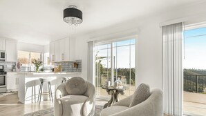 Een moderne keuken met witte kastjes, een eethoek met een barkruk, en een groot raam met uitzicht op de omgeving.