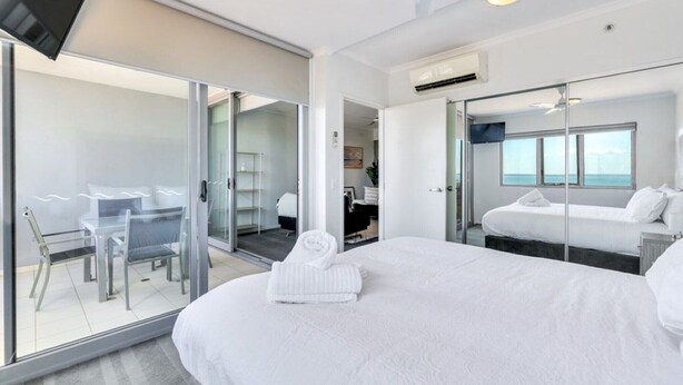 Een moderne hotelkamer met een groot bed, een glazen deur naar een balkon, een kleine tafel met stoelen en een aan de muur bevestigde televisie.