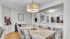 Una cucina moderna con zona pranzo, che include un tavolo di legno, sedie, una lampada a sospensione, un frigorifero e un gioco a parete.