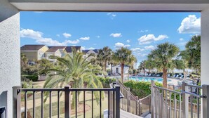 Un balcone con vista su una piscina, palme e case sullo sfondo.