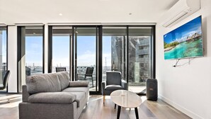 Una sala de estar moderna con un sofá gris, una mesita redonda y un ventanal con vistas a la ciudad.
