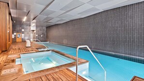 Una piscina interior moderna con una zona de solárium de madera y una pared de azulejos.