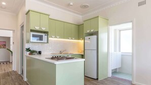 A kitchen with green cabinets, a microwave, a refrigerator, and a small island with a stove. - Sunset Sisters - Lakefront Villas - Forster (Forster)