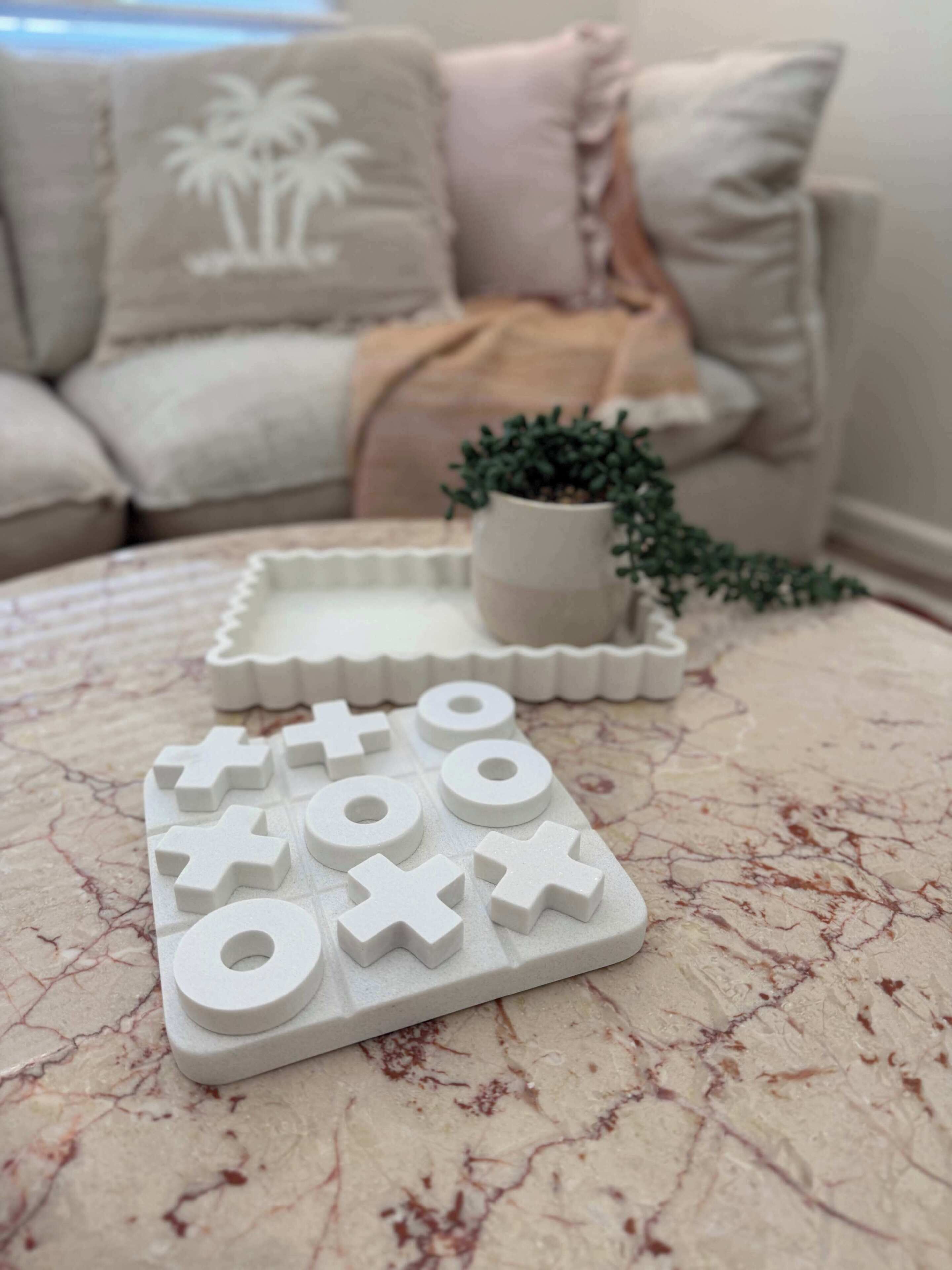 A white cross-shaped puzzle on a textured surface, a small potted plant, and a couch with a palm tree pillow in the background.