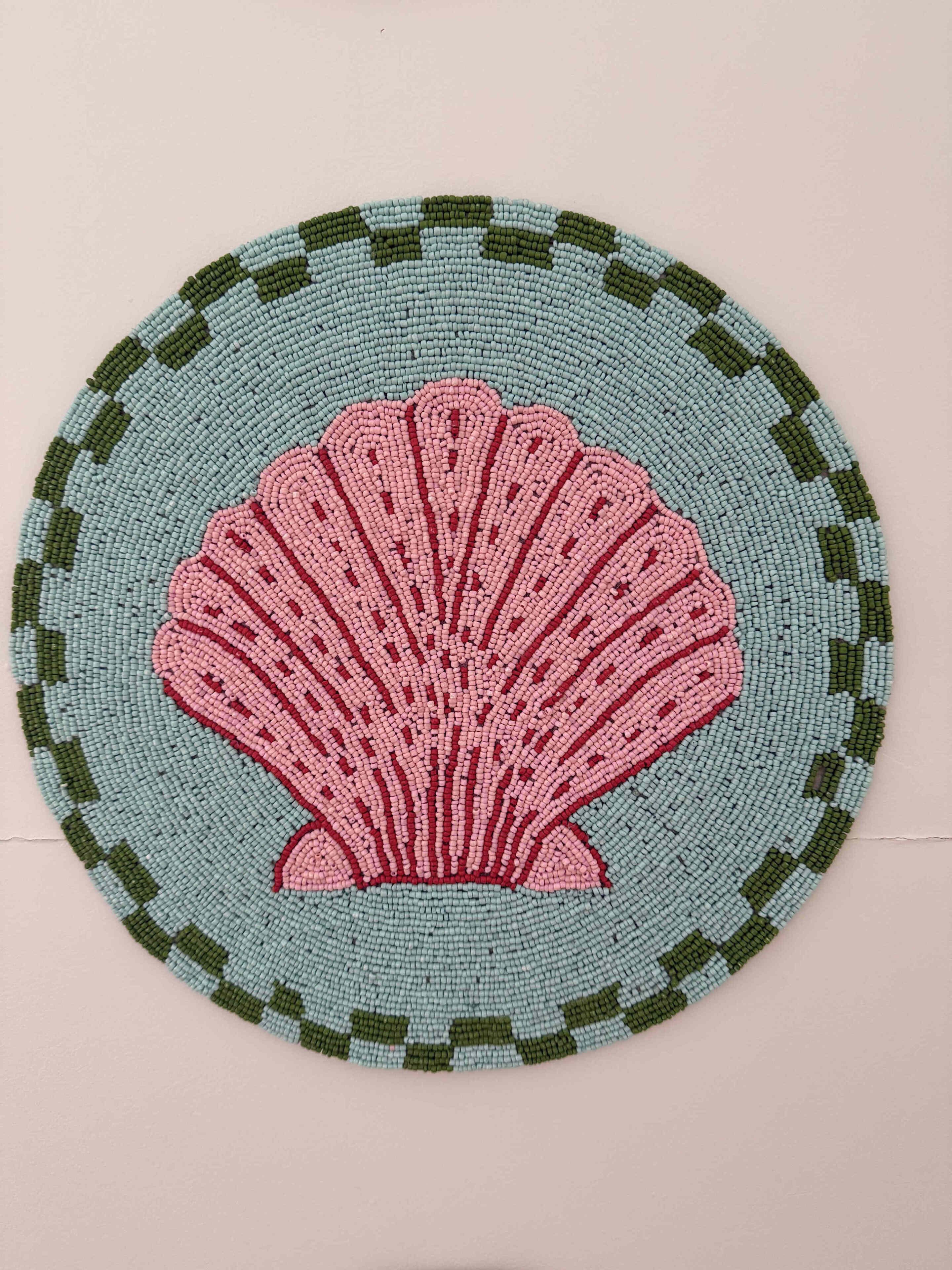 A circular object with a scallop shell design in the center, surrounded by a patterned border.