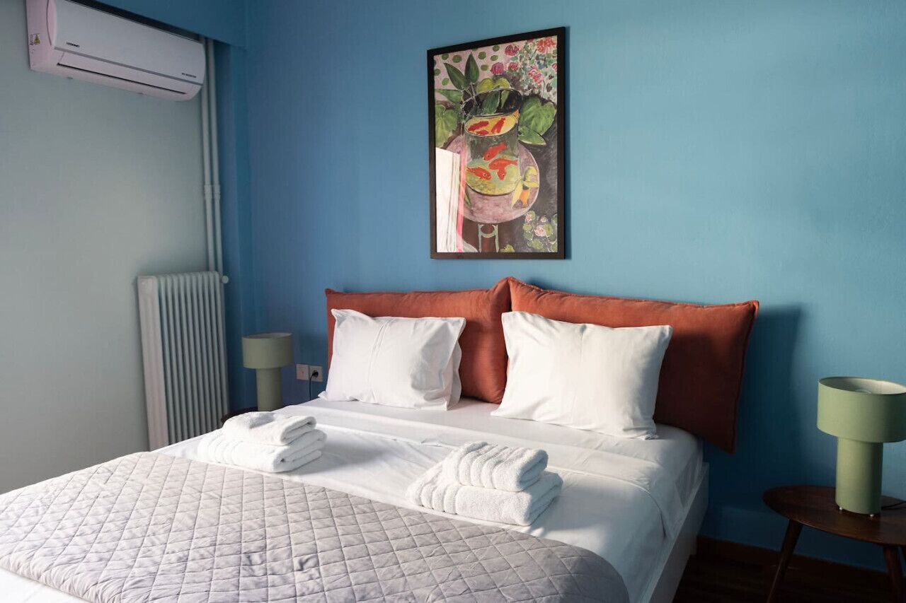 A hotel room with a bed, white bedding, a blue wall, a painting, and a radiator.