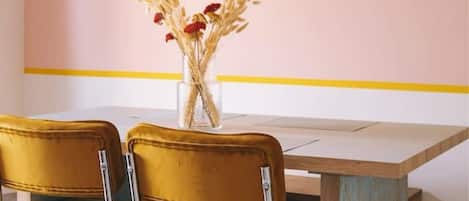 A dining area with a pink wall, a wooden table, and two mustard-colored chairs.