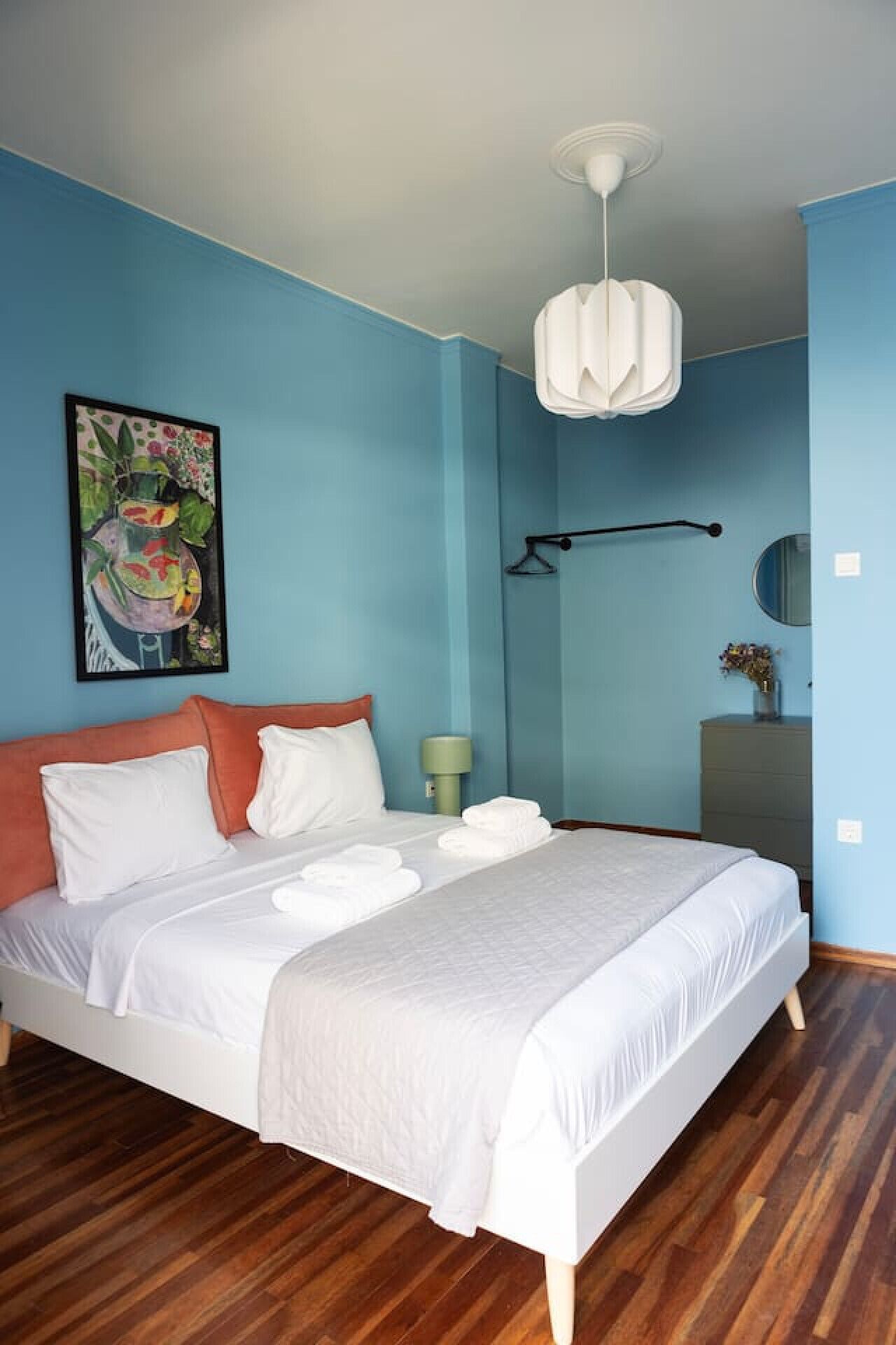 A bedroom with a bed, a painting, a bedside lamp, a dresser, and a mirror.