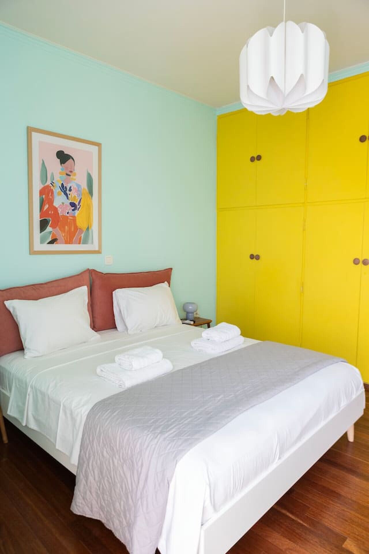 Une chambre à coucher avec un lit, une table de chevet, un tableau et une armoire jaune.
