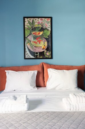 A bed with white bedding and pillows, a quilted mattress, and a framed painting of a fish tank on the wall. - Vibrant Retreat Funky Style & Acropolis View! (Athina)