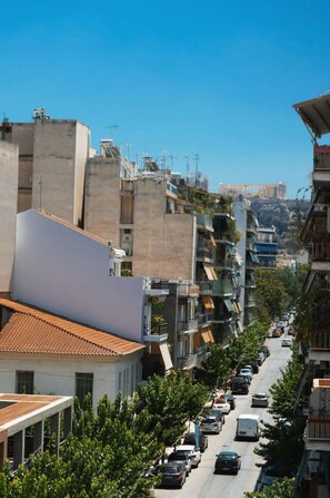 A narrow urban street lined with multi-story buildings, featuring balconies and a clear view of a distant historical landmark. - Vibrant Retreat Funky Style & Acropolis View! (Athina)