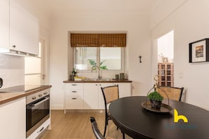 A compact kitchen with white cabinets, a wooden countertop, and a dining area with a black table and chairs. - Modern Family Apt with Courtyard near Acropolis! (Athina)