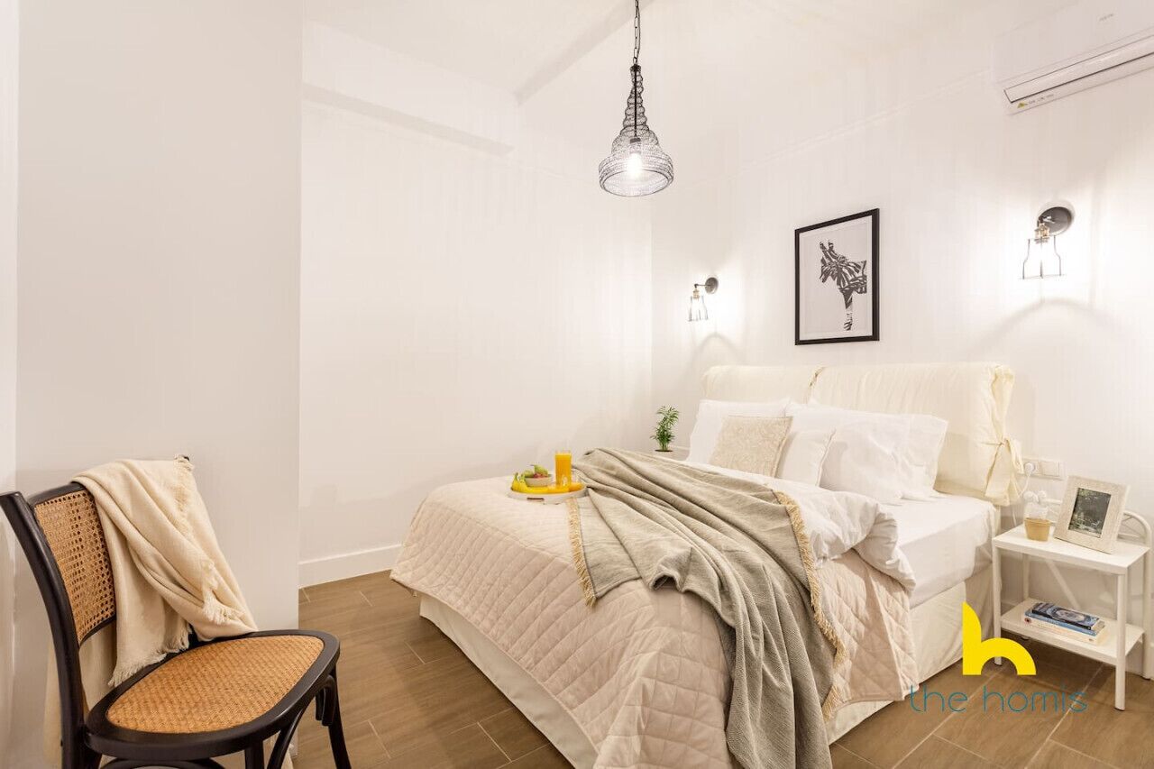 A minimalist bedroom with a bed, bedside table, chair, and a hanging light fixture.