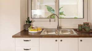 Eine Küche mit doppelter Spüle, einem Fenster mit Bambusrollo, einem weißen Schrank mit Schubladen und einer Obstschale auf der Arbeitsplatte.