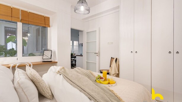 Ein Schlafzimmer mit einem Bett, einem Nachttisch mit Frühstücksangebot, einem Kleiderschrank und einem Fenster mit Jalousien.