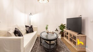 Ein modernes Wohnzimmer mit einer Couch, einem Glastisch, einem Fernseher und einem Holzkasten.