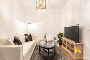 Ein modernes Wohnzimmer mit einer Couch, einem Glastisch, einem Fernseher und einem Holzkasten.