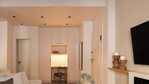 A hotel room with a bed, a desk with a chair, a TV mounted on the wall, and a fireplace. - Luxurious Zen Retreat W/Balcony & 300mbps WiFi (Athina)
