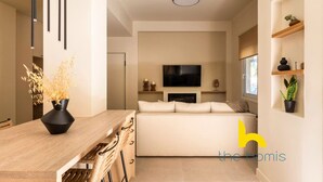 A modern living room with a sofa, a flat-screen TV, and a dining area with a wooden table and chairs. - Luxurious Zen Retreat W/Balcony & 300mbps WiFi (Athina)