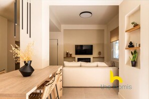 A modern living room with a sofa, a flat-screen TV, and a dining area with a wooden table and chairs. - Luxurious Zen Retreat W/Balcony & 300mbps WiFi (Athina)