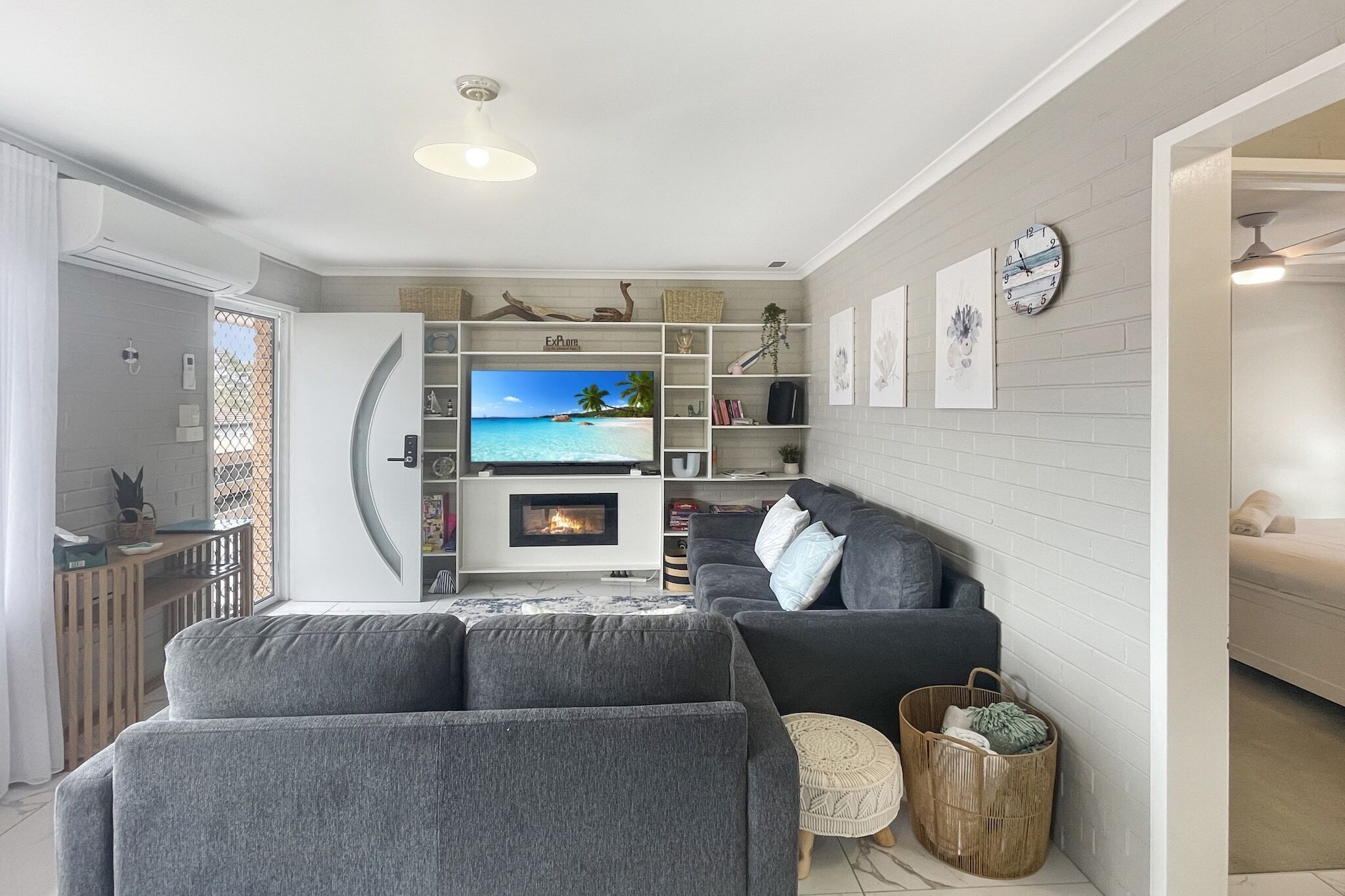 Ein modernes Wohnzimmer mit Kamin, grauen Sofas, einem Fernseher und einem Bücherregal.