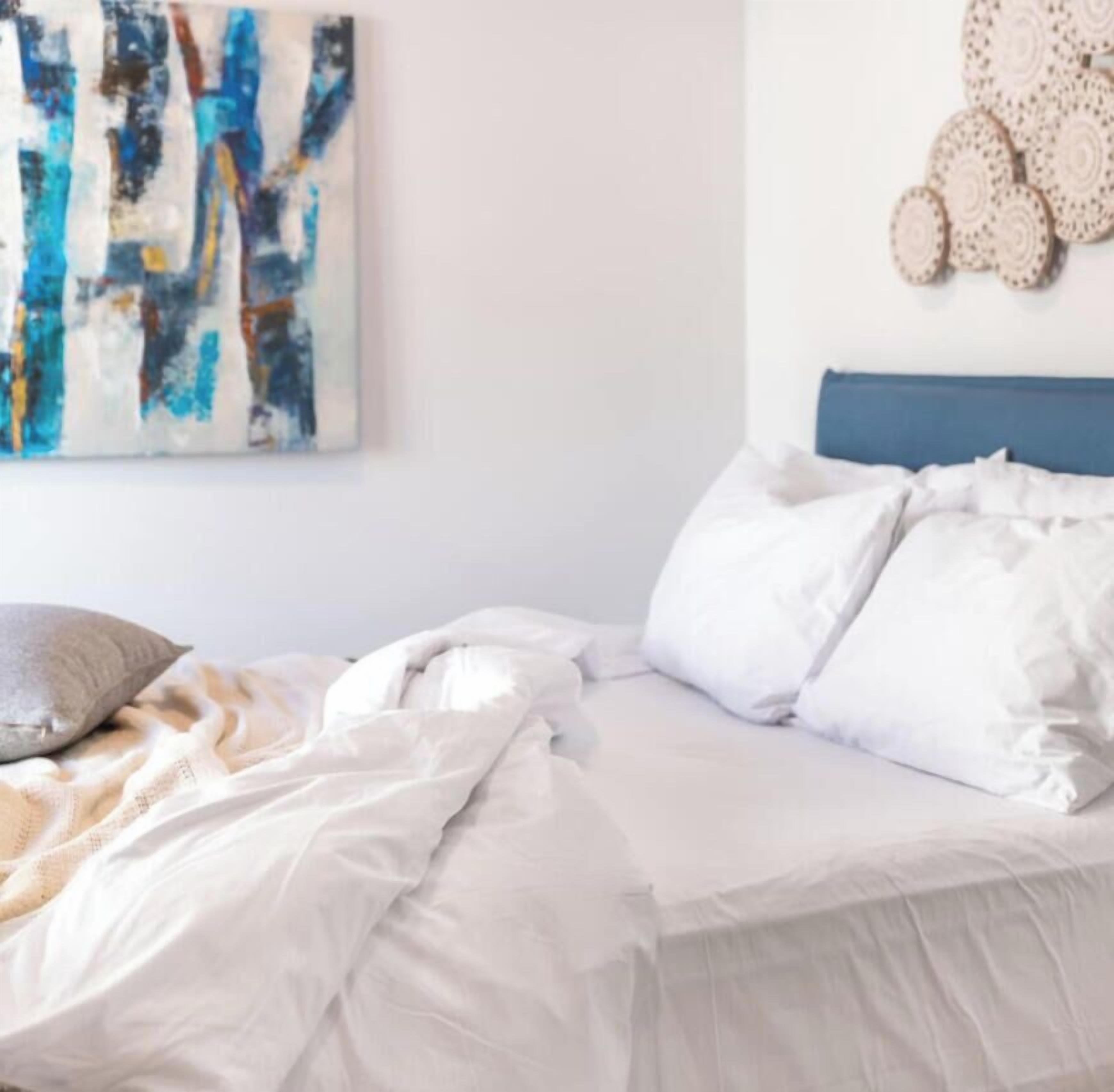 Un dormitorio con cama, almohadas, una colcha, una obra de arte en la pared y decoración de pared.