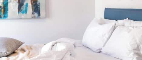 Un dormitorio con cama, almohadas, una colcha, una obra de arte en la pared y decoración de pared.