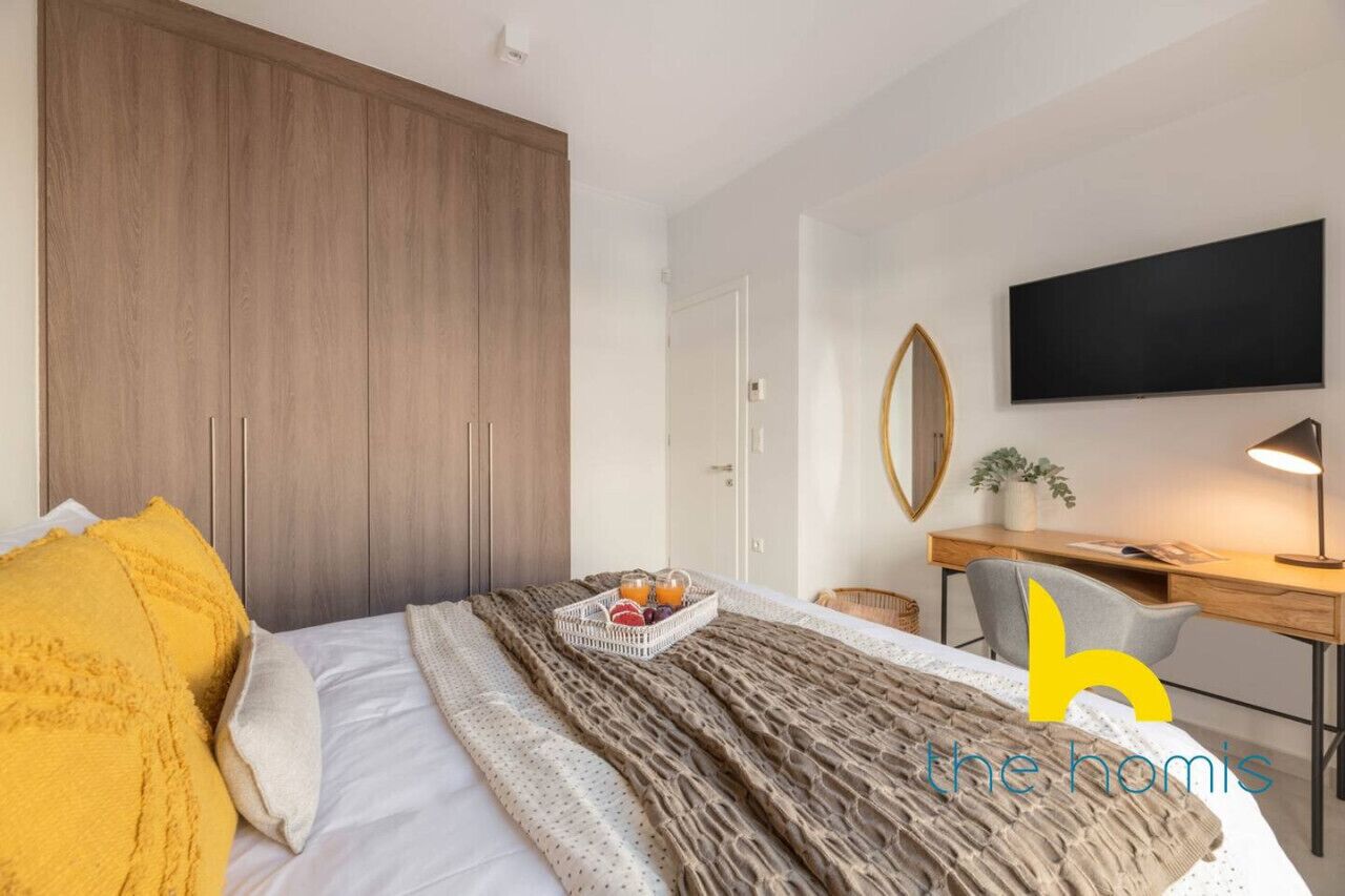Une chambre d’hôtel moderne avec un grand lit, une armoire en bois, un bureau avec une chaise, une télévision et une petite plante en pot.