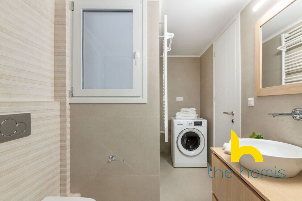 A modern bathroom with a built-in washing machine, a sink, and a mirror.
