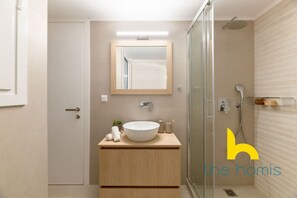 Une salle de bain moderne avec un grand miroir, un lavabo rond et une douche à parois de verre.