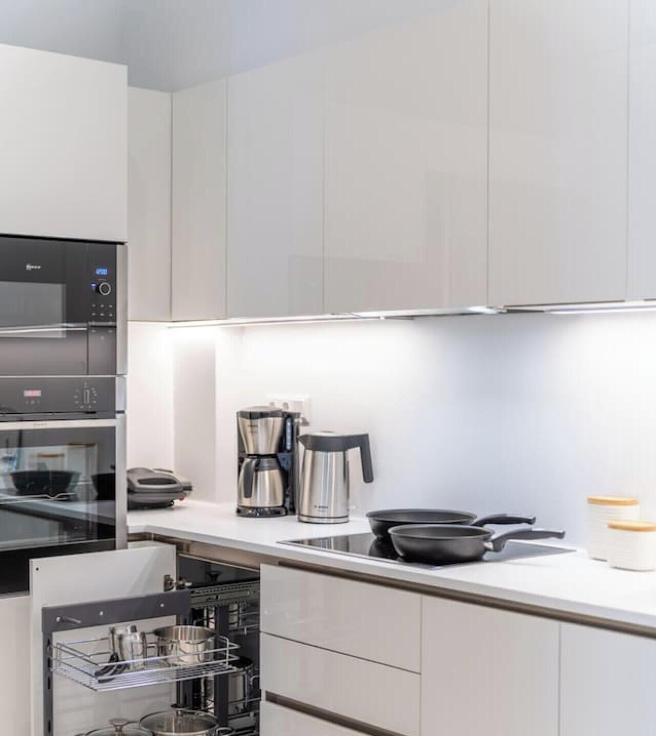 A modern kitchen with stainless steel appliances, including a coffee maker and a kettle, and a built-in oven.