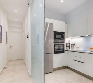 A modern kitchen with stainless steel appliances, white cabinetry, and a glass partition. - Upscale central APT, Patio near Hospitals & Metro (Μενεμένη)