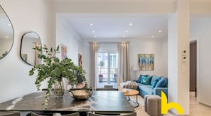 A modern living room with a dining area, featuring a large plant, a sofa, and a coffee table. - Upscale central APT, Patio near Hospitals & Metro (Μενεμένη)