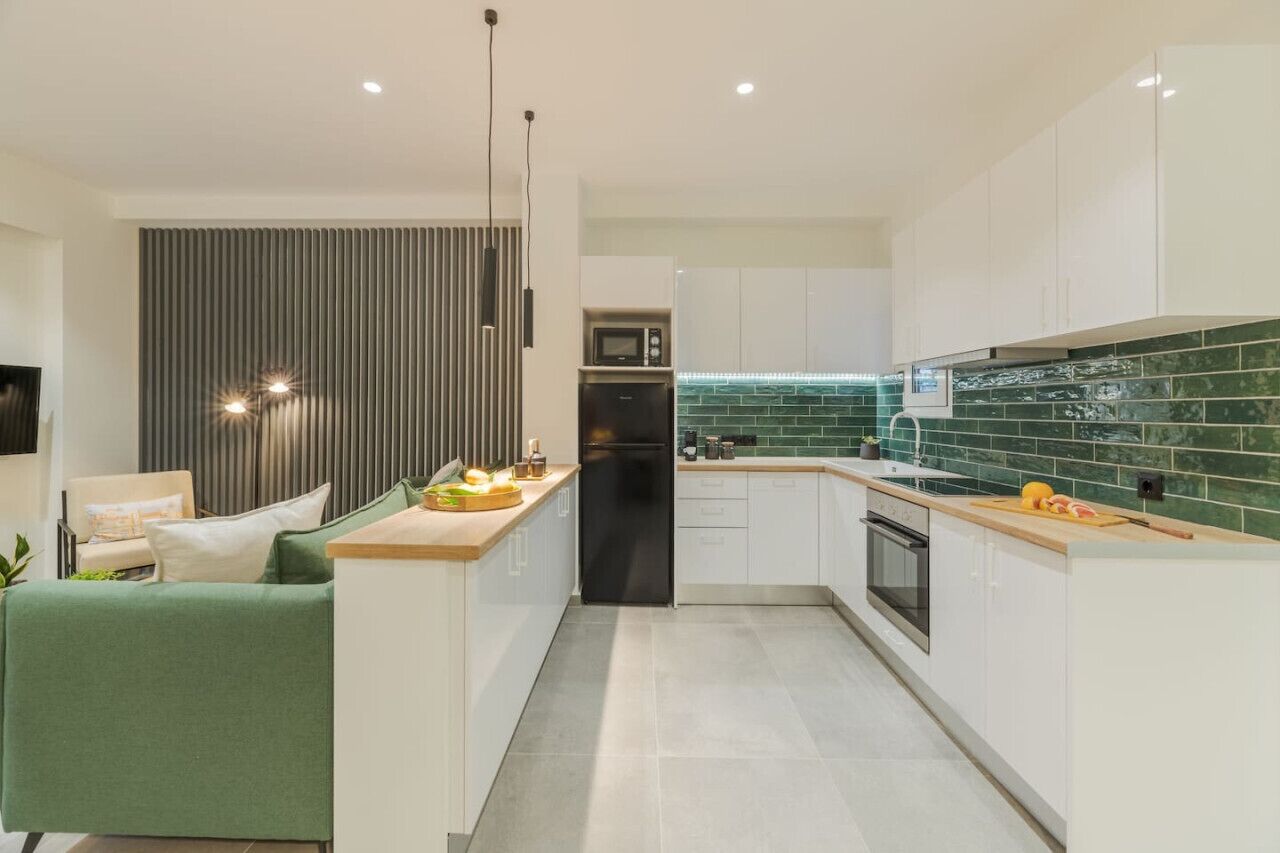 Una cocina moderna con armarios blancos, un salpicadero verde y una isla central con microondas y horno.