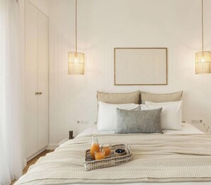 Een slaapkamer met een bed, twee bedlampen, een ingelijst beeld aan de muur en een dienblad met drankjes op het bed.