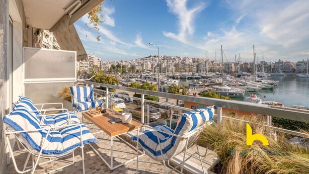 Varanda com área de estar ao ar livre, vista para um porto de iates e paisagem urbana ao fundo.