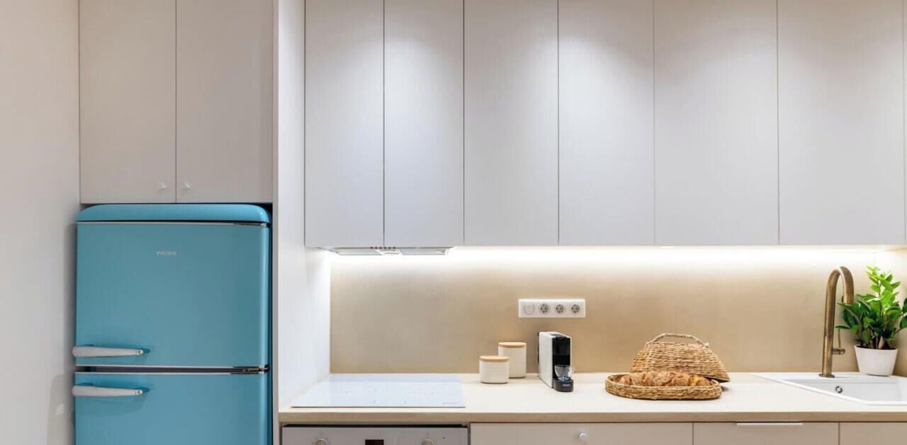 A modern kitchen with a blue refrigerator, a coffee maker, and a basket of bread on the counter.