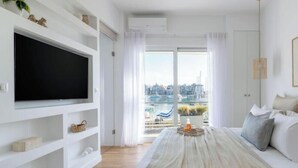 Quarto moderno com uma cama grande, uma TV fixada em uma parede branca e vista para uma marina pela janela.