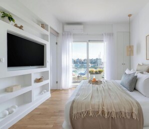 Une chambre moderne avec un grand lit, un téléviseur fixé au mur blanc et une vue sur une marina, visible par la fenêtre.